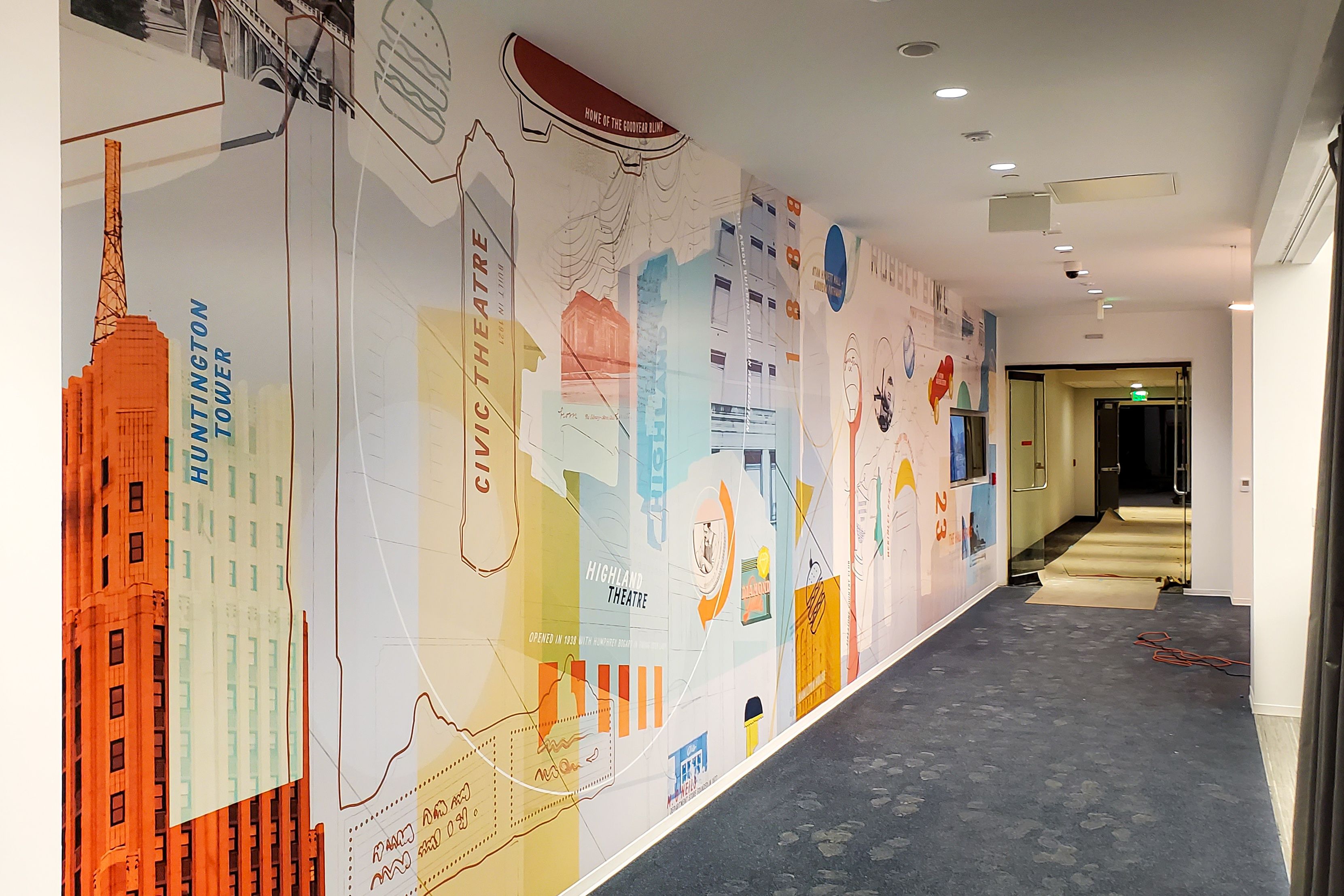 A large, abstract, printed wall graphic of various Akron, OH themed items decorates the wall of a corporate office.