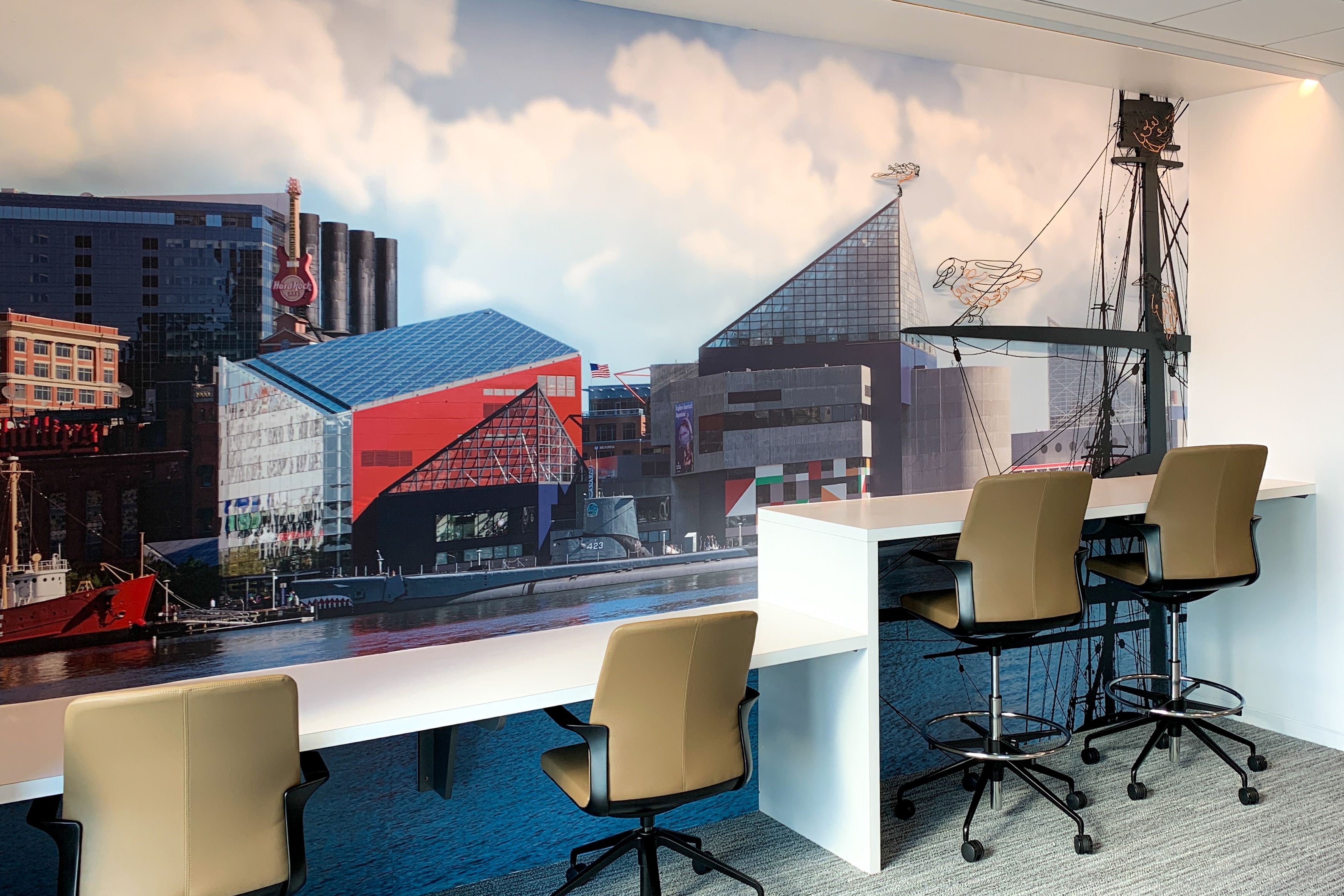 A printed wall graphics decorates a wall with a desktop. The graphics shows the Baltimore, MD skyline and features bent-wire shapes of orange and black Orioles.
