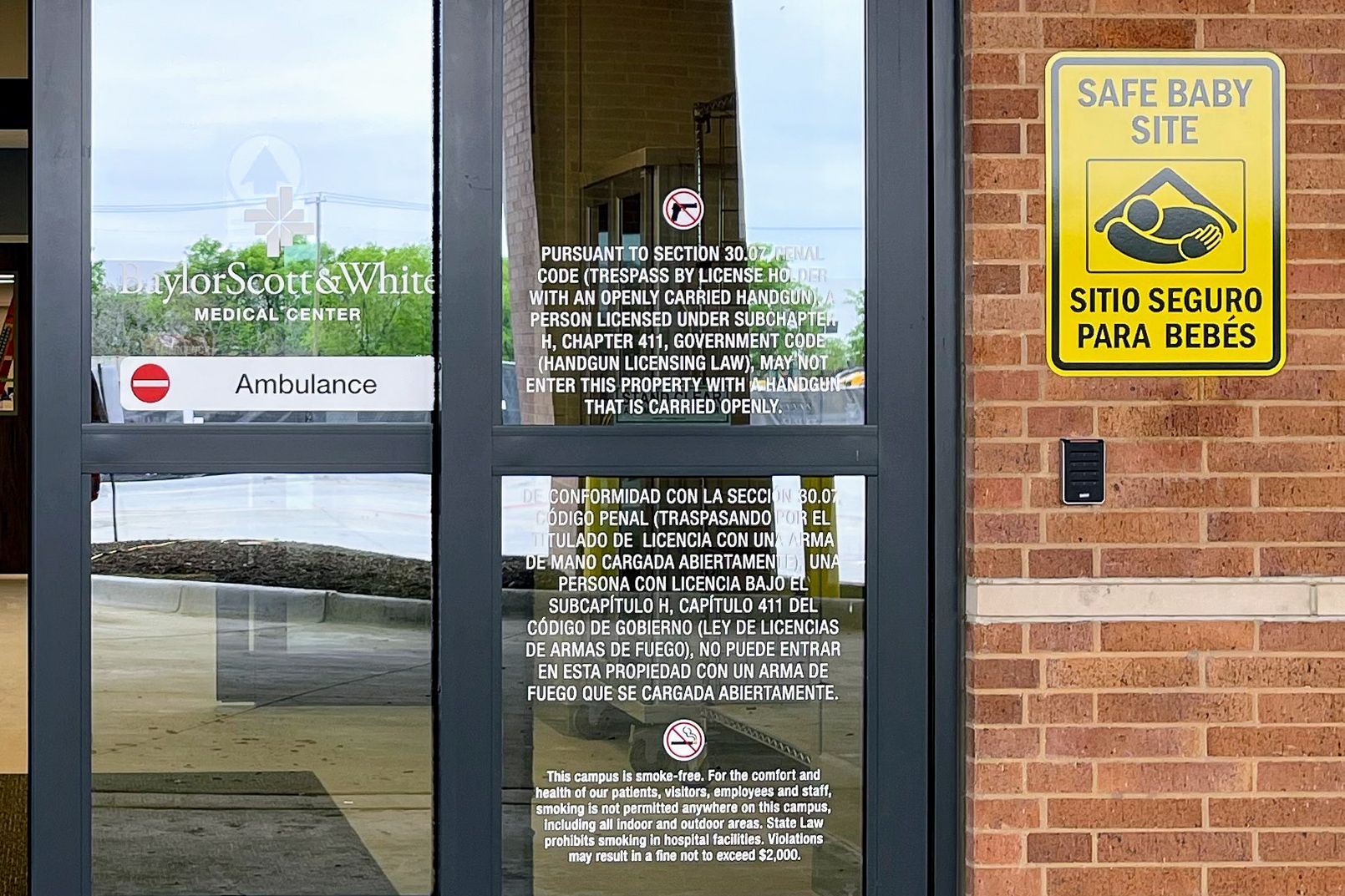 A tactile "FLUORO" room sign is mounted outside a radiology room. Above it is a yellow sign with a purple radiation symbol and text warning about radiation.
