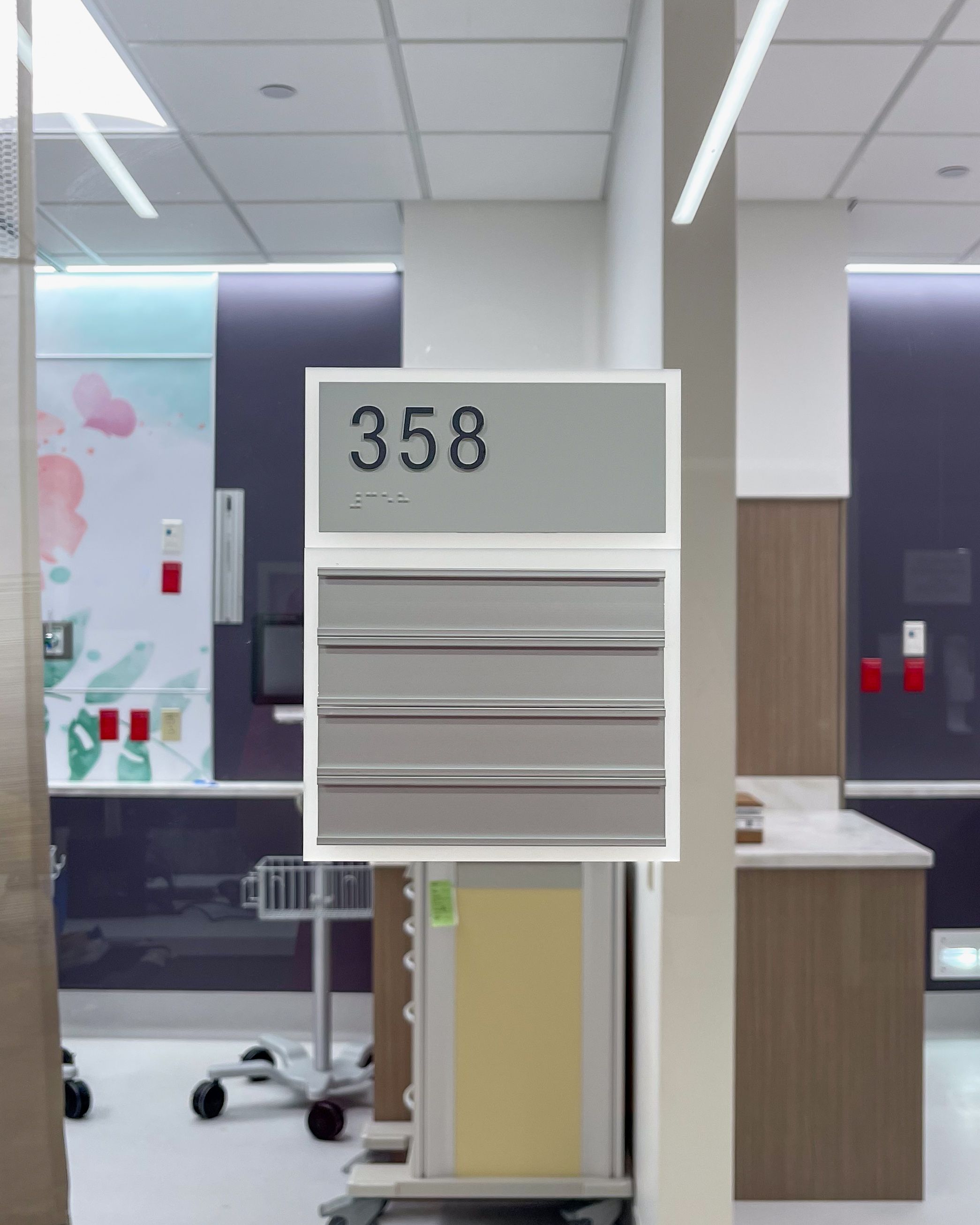 A silver tactile room sign labels patient room 358 in a hospital. It has a frosted white border and 4 aluminum channels for changeable inserts.