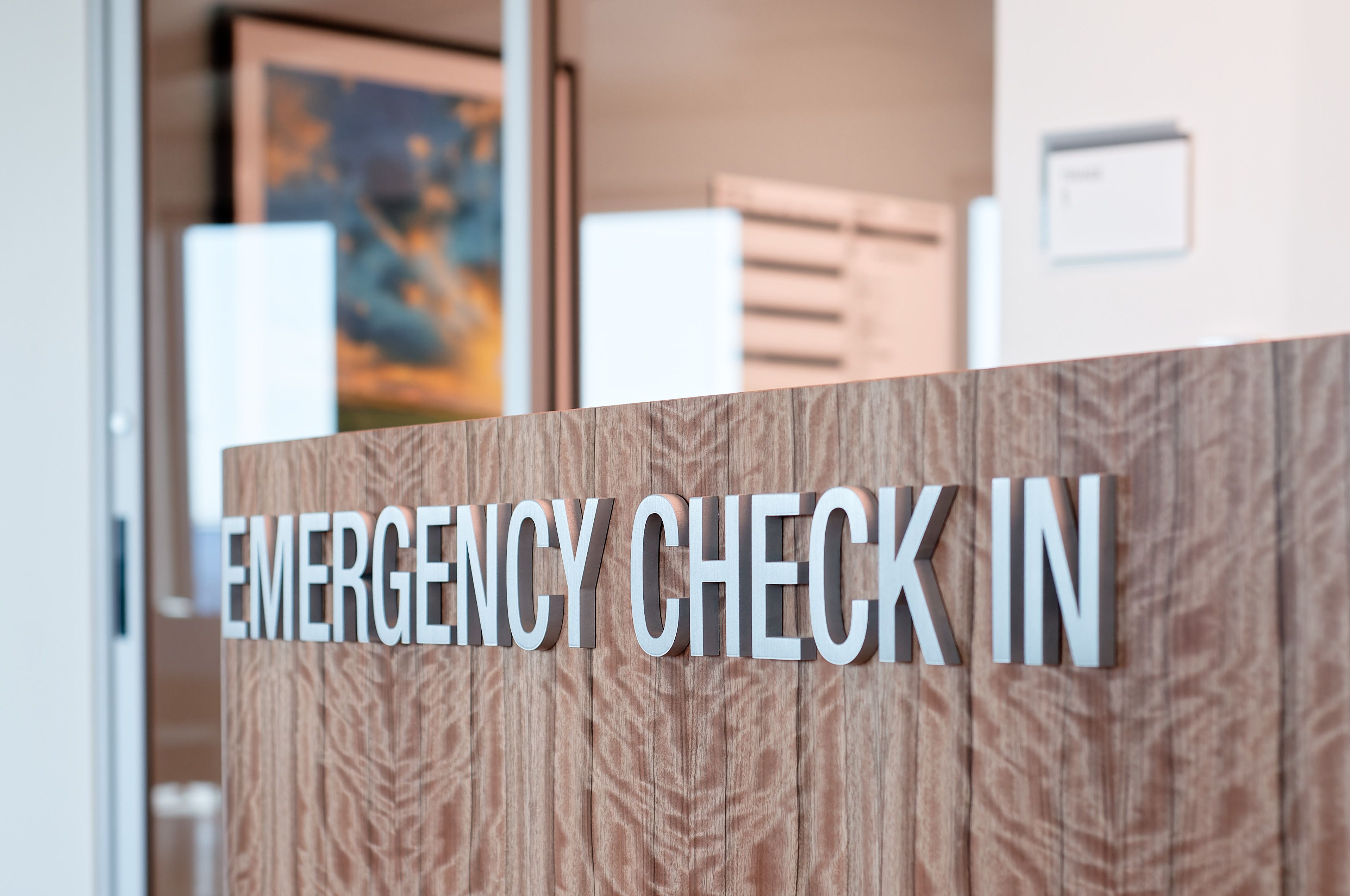 A set of silver acrylic letters mounted on the front of a wooden desk spell out "EMERGENCY CHECK-IN".