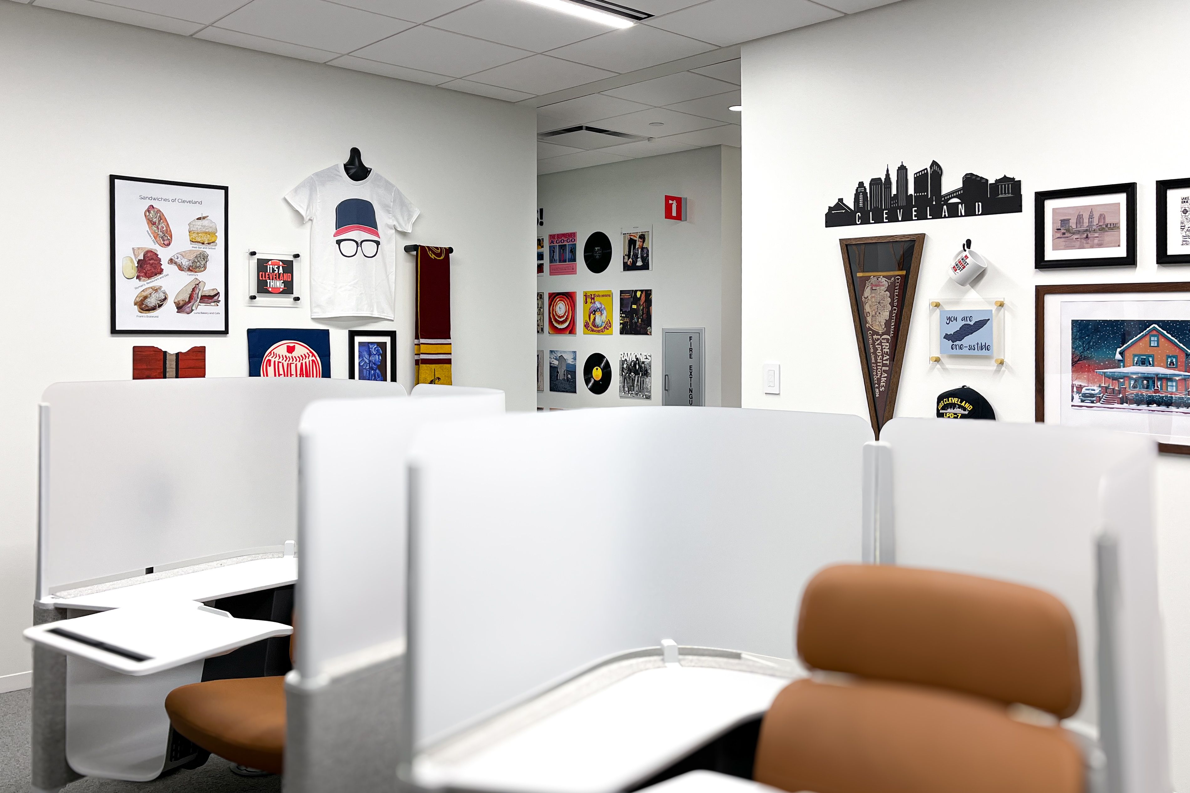 Several walls in a small office are decorated with groupings of Cleveland memorabilia, such as music albums, a skyline, sports-themed items, and various pieces of art.