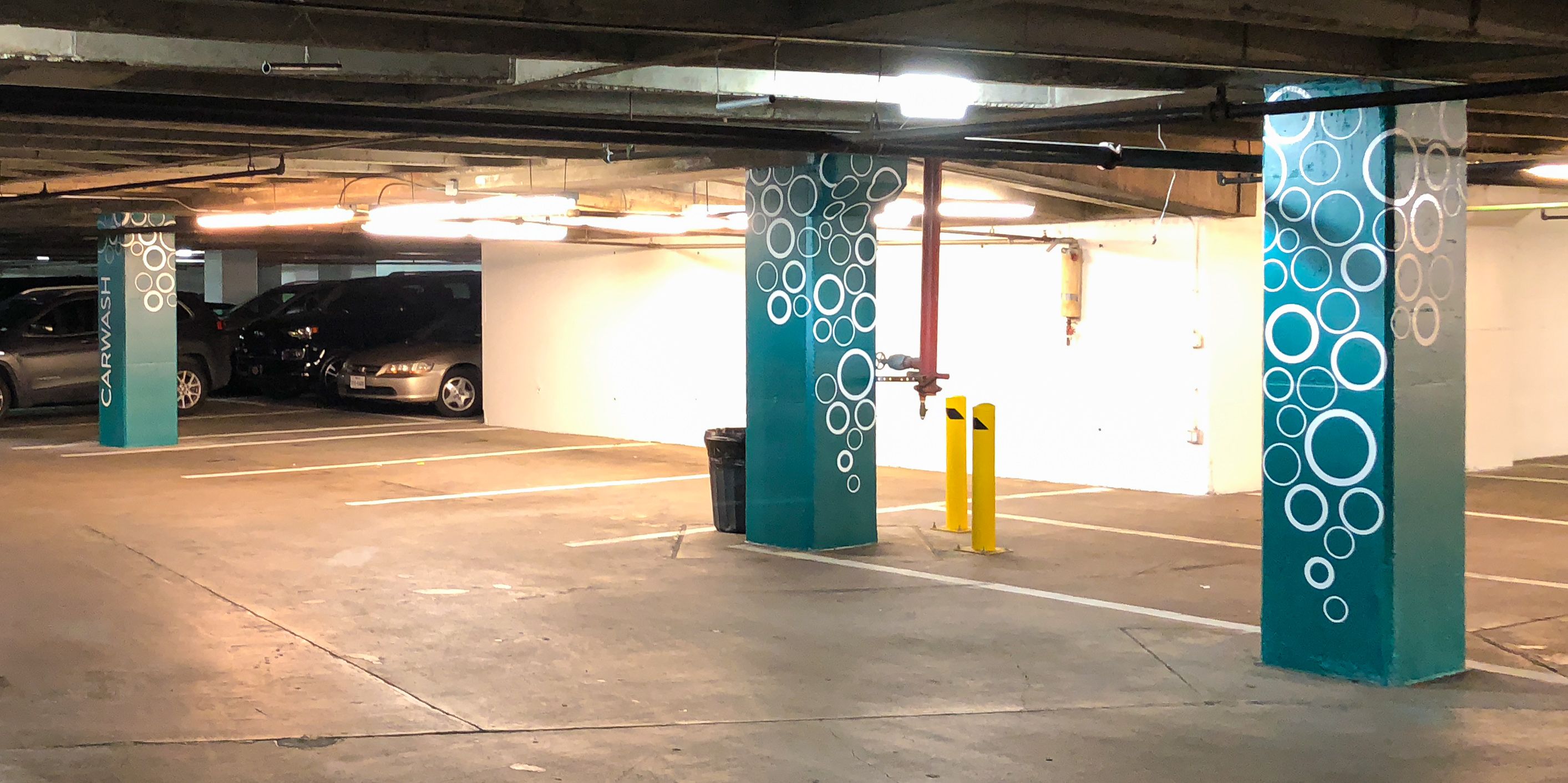 Green concrete columns in a parking garage are decorated with white cut vinyl bubbles and "CARWASH" lettering.