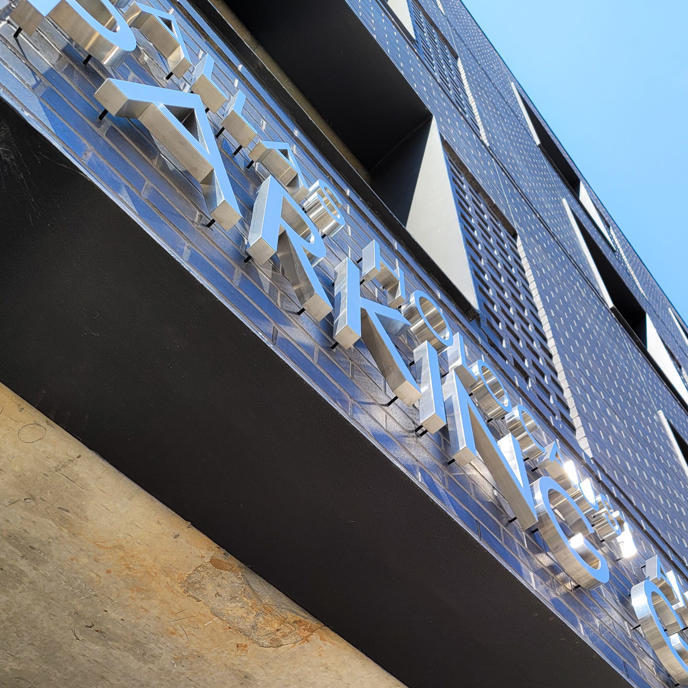 Stainless steel dimensional letters are mounted to a black brick wall above the entry to a parking garage.