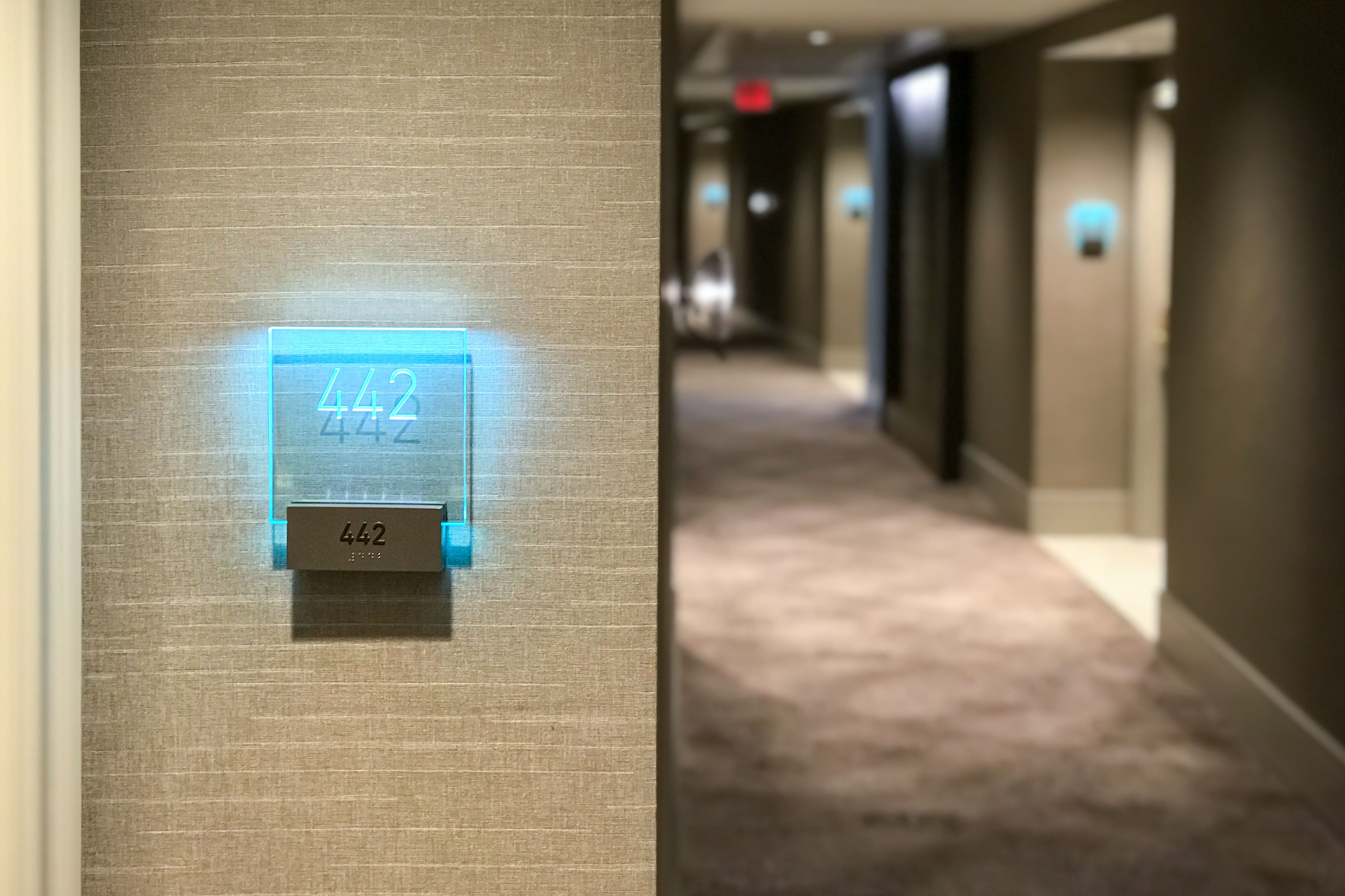 A tactile room sign with a glowing acrylic panel etched with room number 442 on the wall outside of a hotel room.