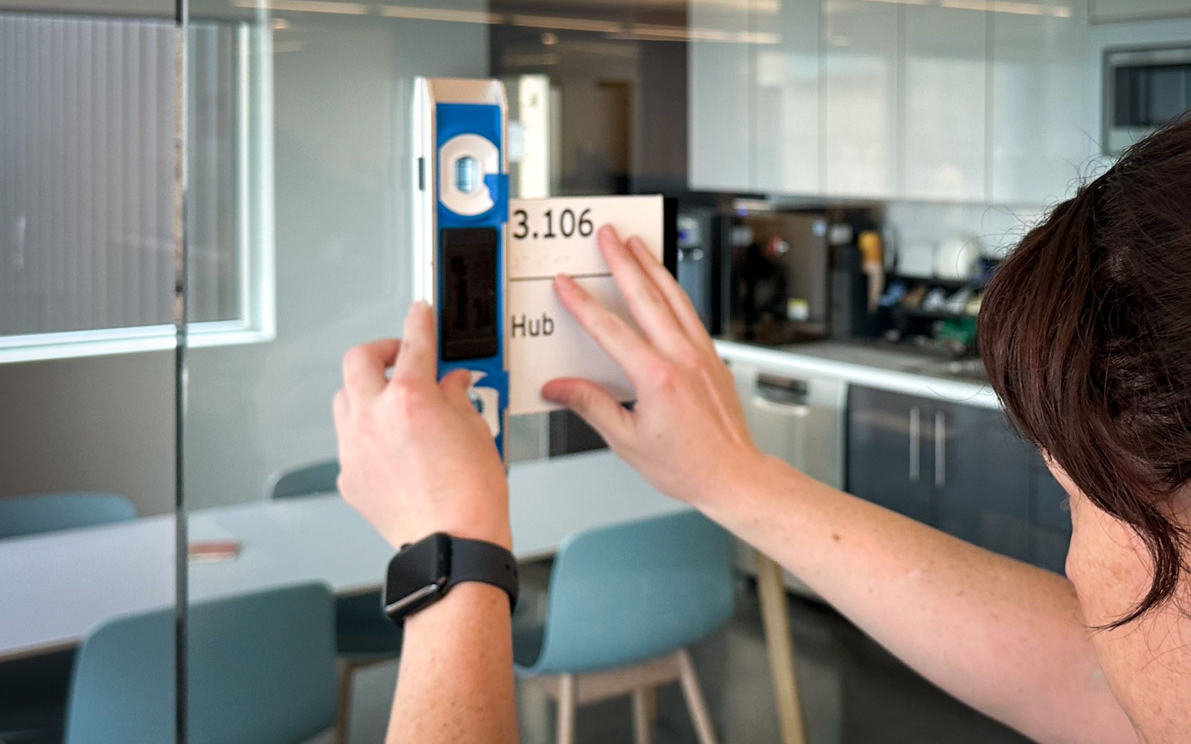 A sign installer is applying an ADA room sign to a glass window using a level to ensure it is straight.