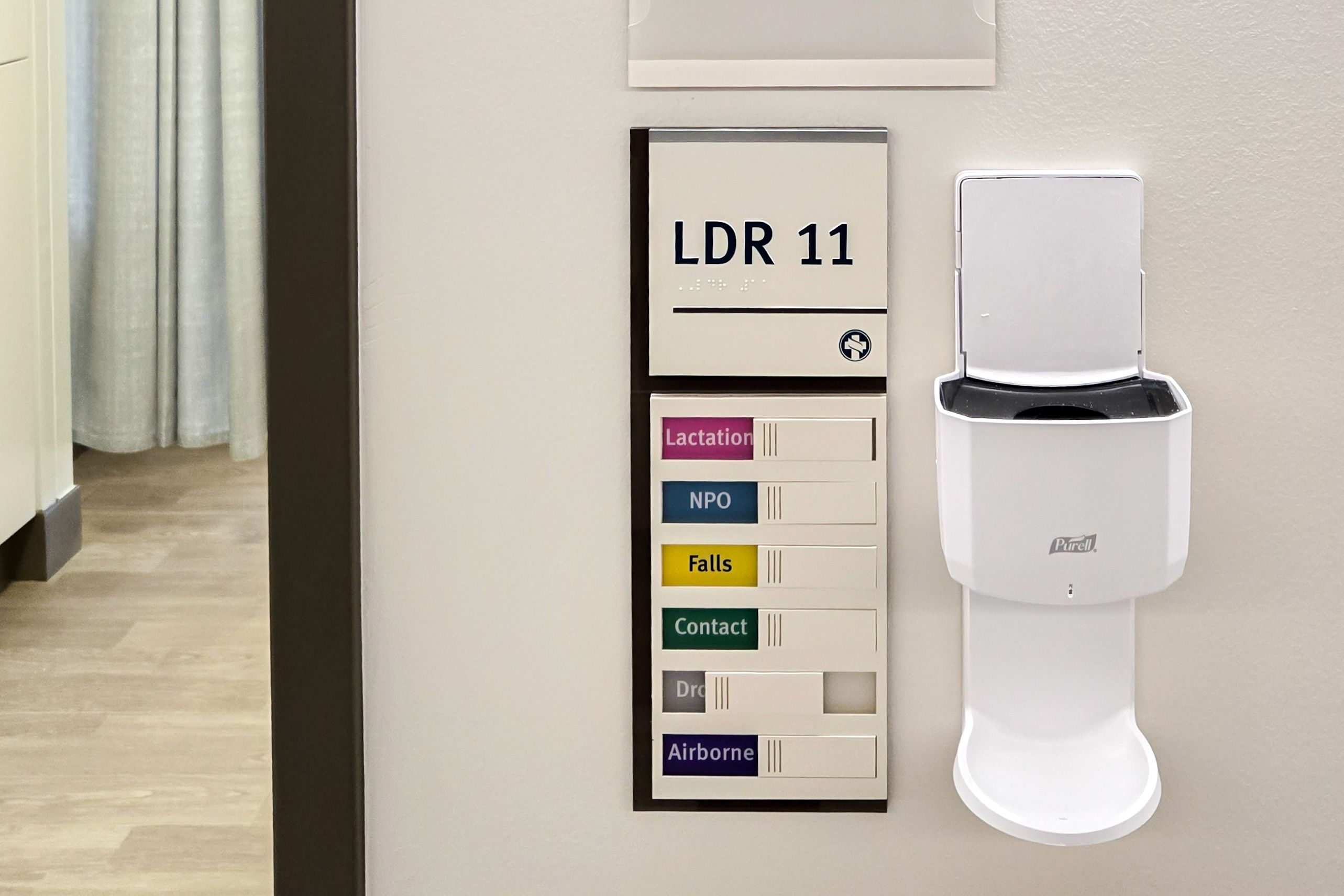 A sign mounted above an elevator call button in a hospital shows a printed fire evacuation plan and states to use the stairs in case of fire. It's accented with a light blue laser etched patterned acrylic panel and brown header.