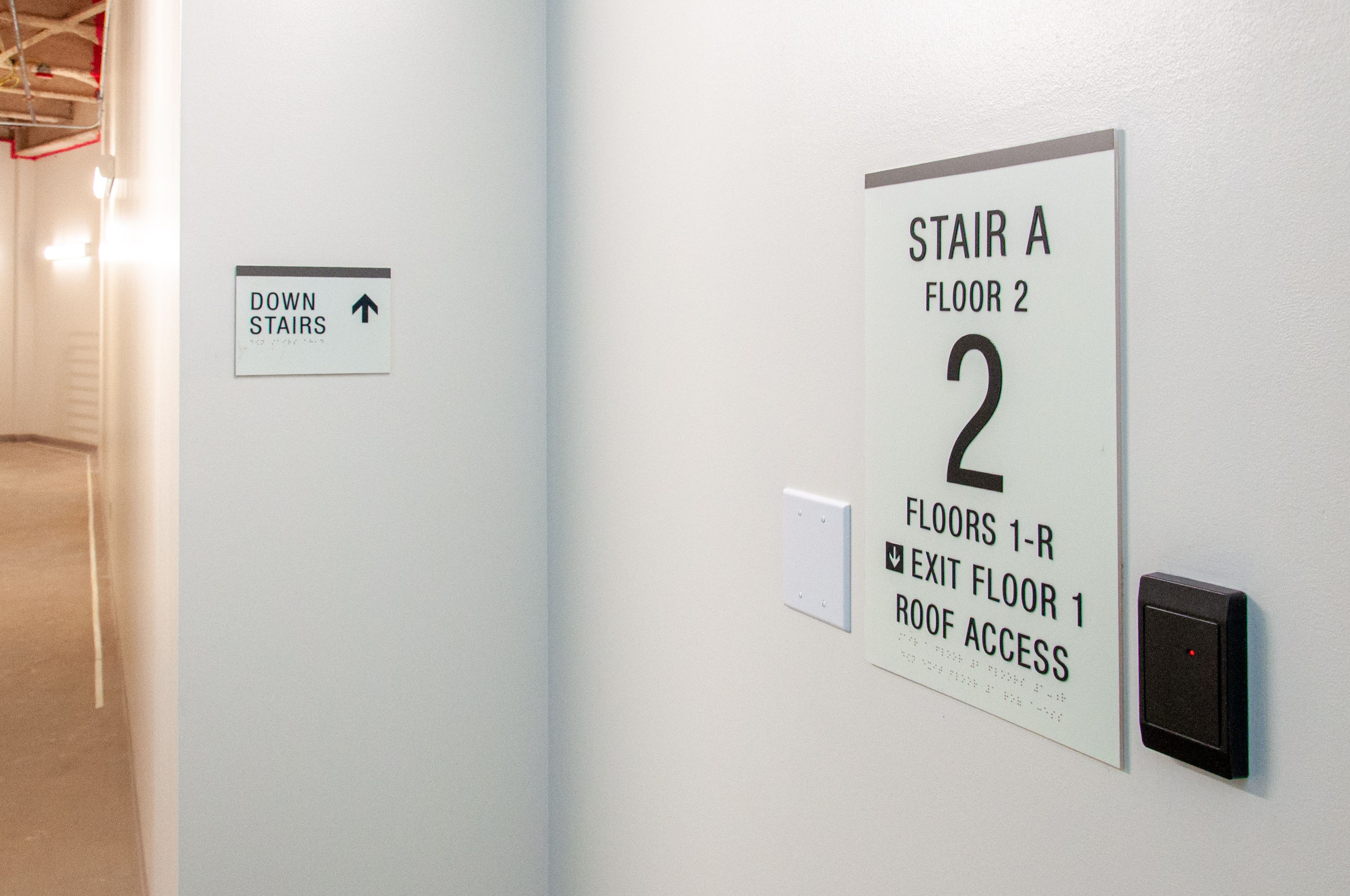 Two glow-in the dark signs are mounted inside a stairwell. One sign shows the floor and egress information and the other indicates the direction to the nearest stairs.