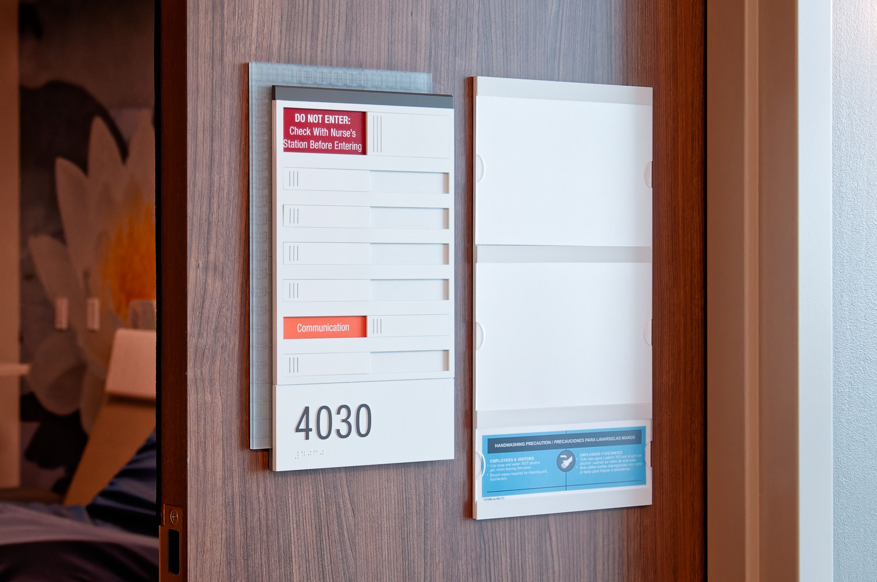 A patient room sign with a tactile room number, braille, and patient notice sliders, next to an replaceable insert sign.