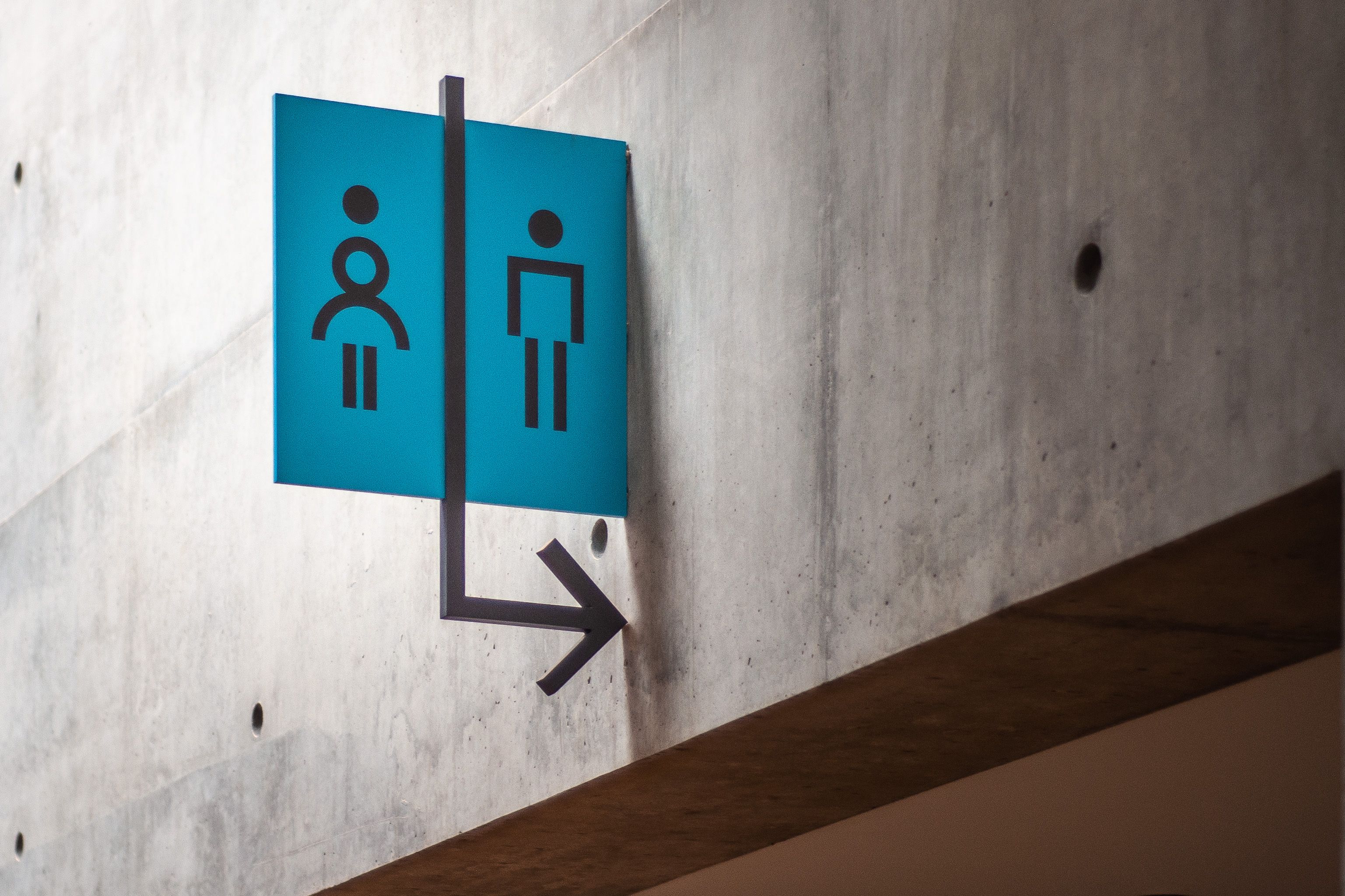 A flag sign with restroom symbols and an arrow project from a concrete wall in a museum.