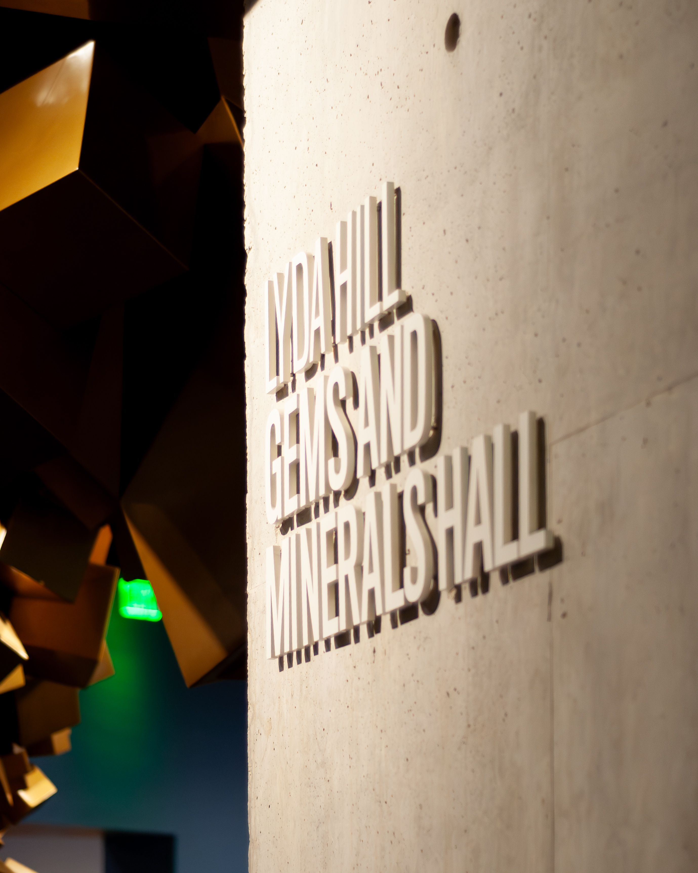 White dimensional letters labeling the Mineral Hall in a museum stand off from a concrete wall.