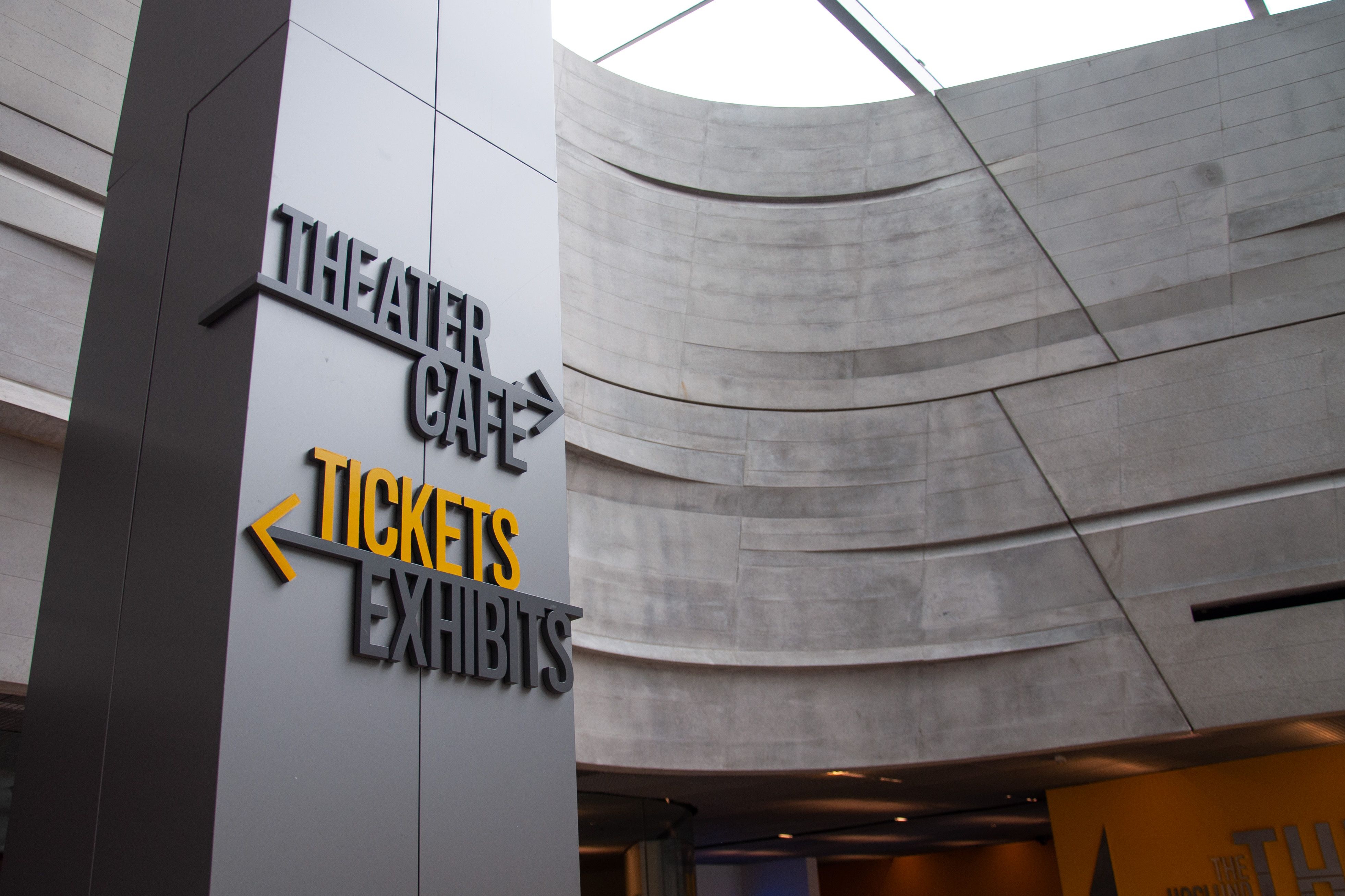 Aluminum dimensional letters and arrows wrap around a column in a dramatic museum atrium, pointing to various destinations.