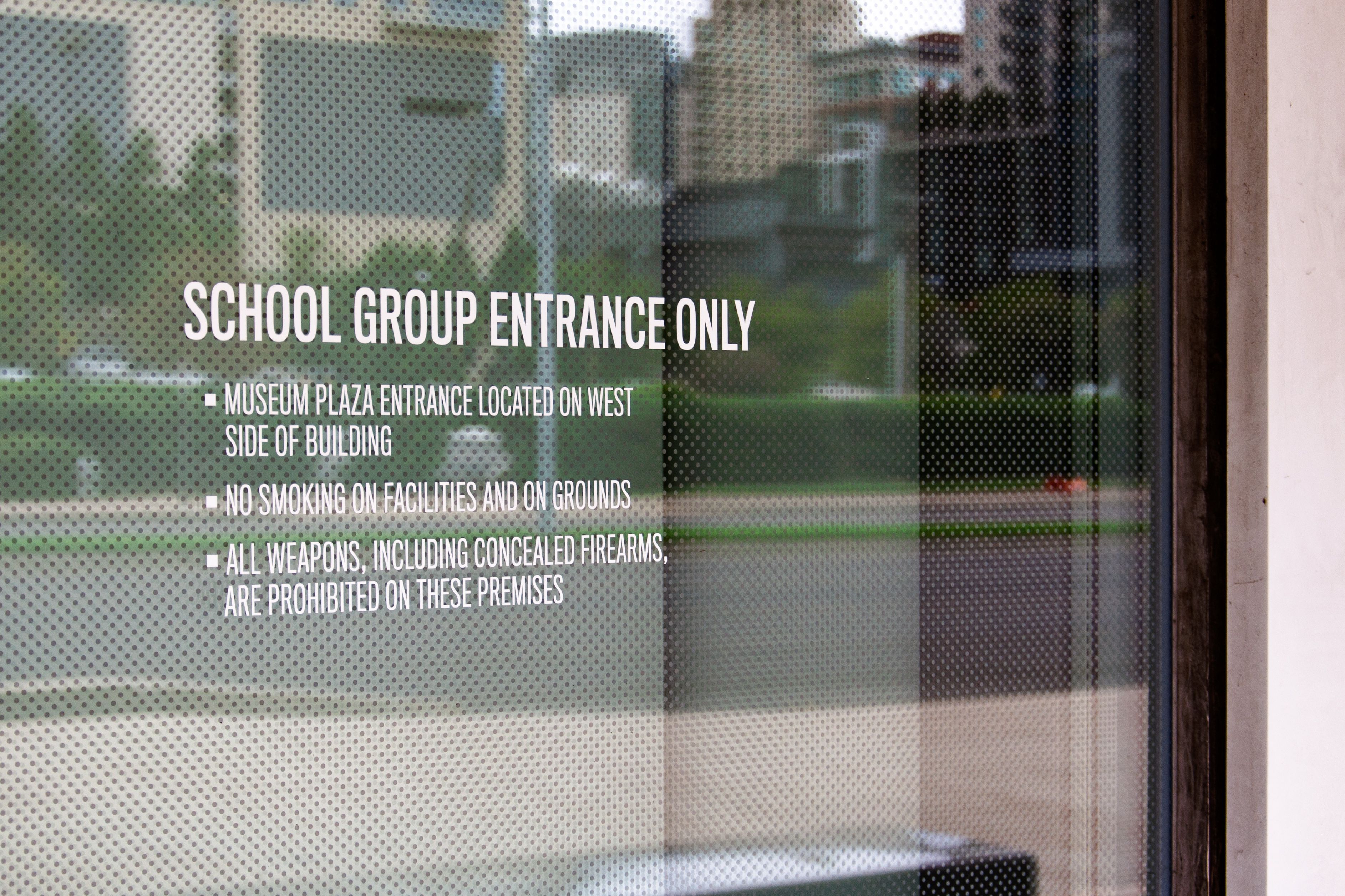 Cut white vinyl text on a window indicates a school group entrance to a museum, along with safety rules and other entrance information.