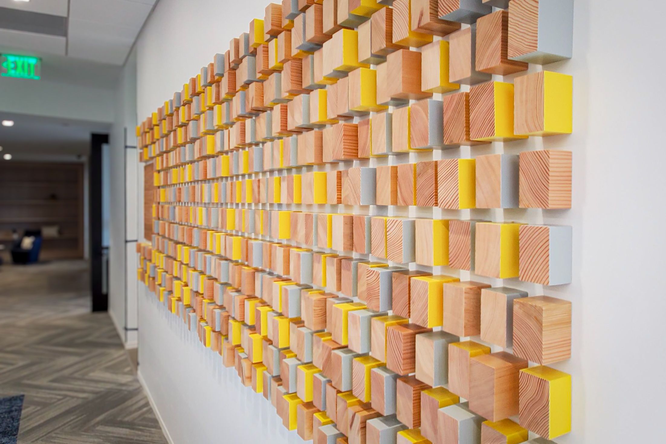 A wall in a corporate office is covered in a grid of wooden blocks of varying thicknesses and edge colors, creating a textured look.