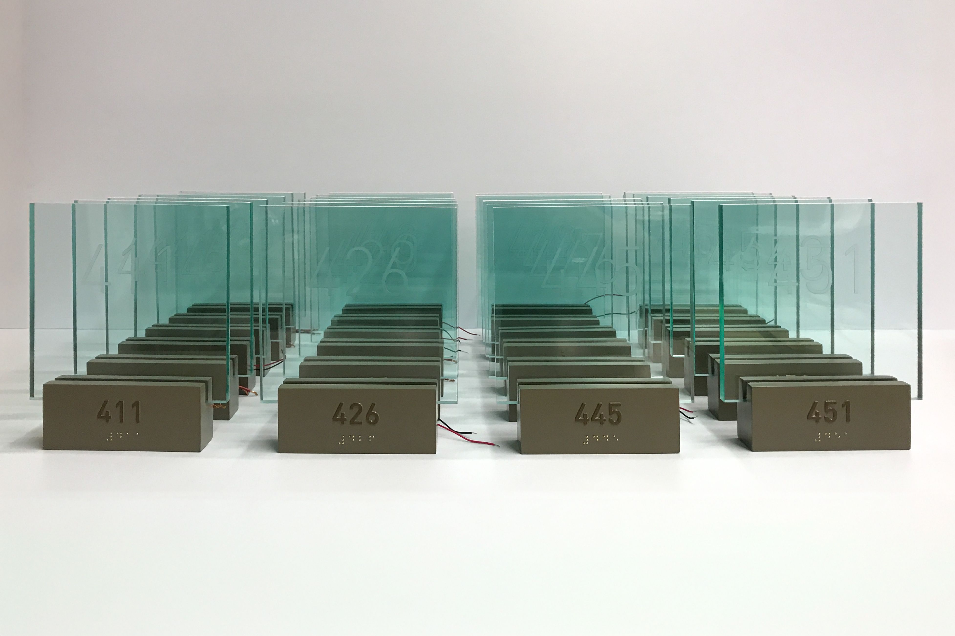 A row of signs laid out on a table for testing, each featuring LED-illuminated acrylic panels etched with room numbers.