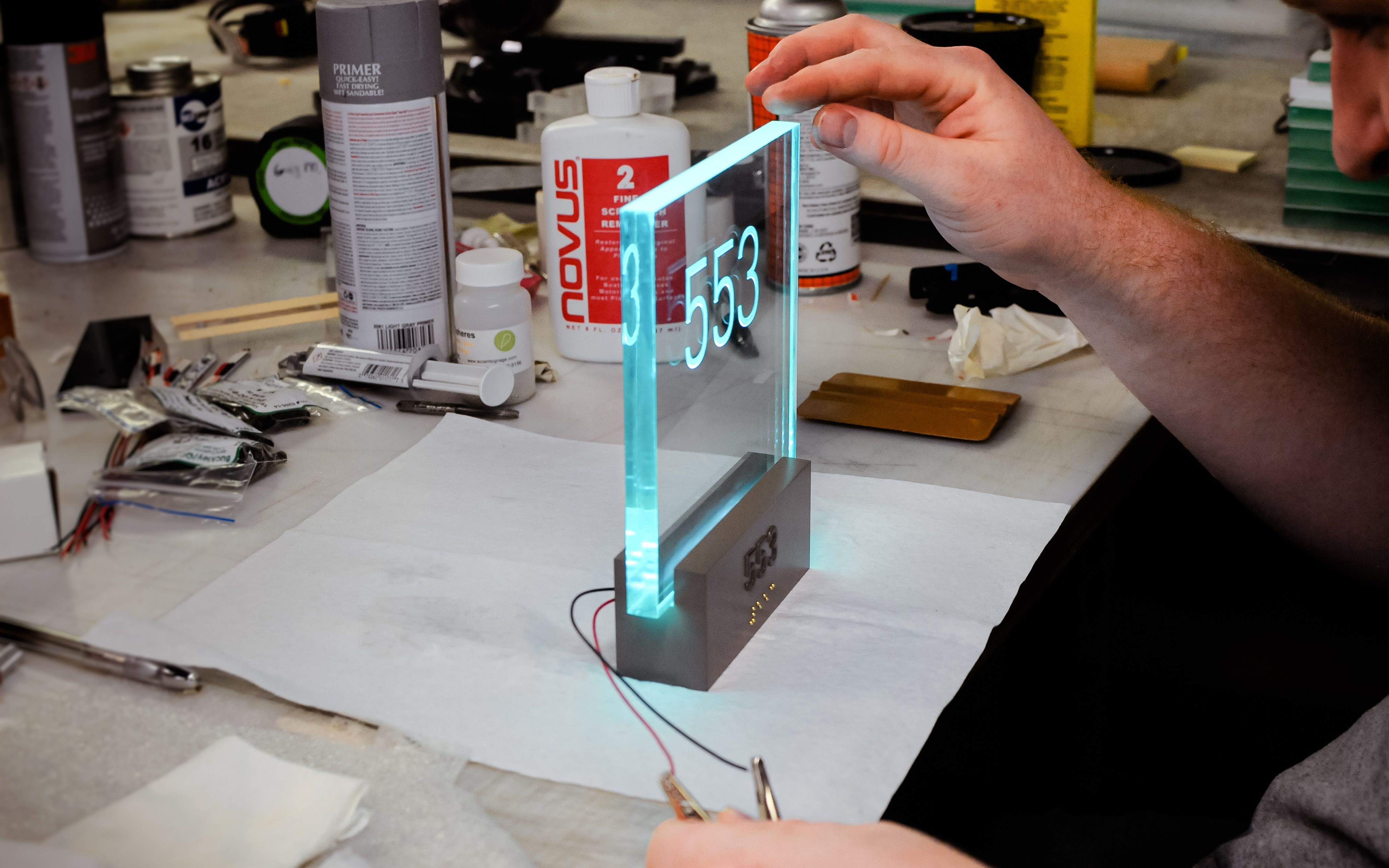 A fabrication team member is inspecting a prototype sign with an illuminated acrylic panel and raised text and braille.