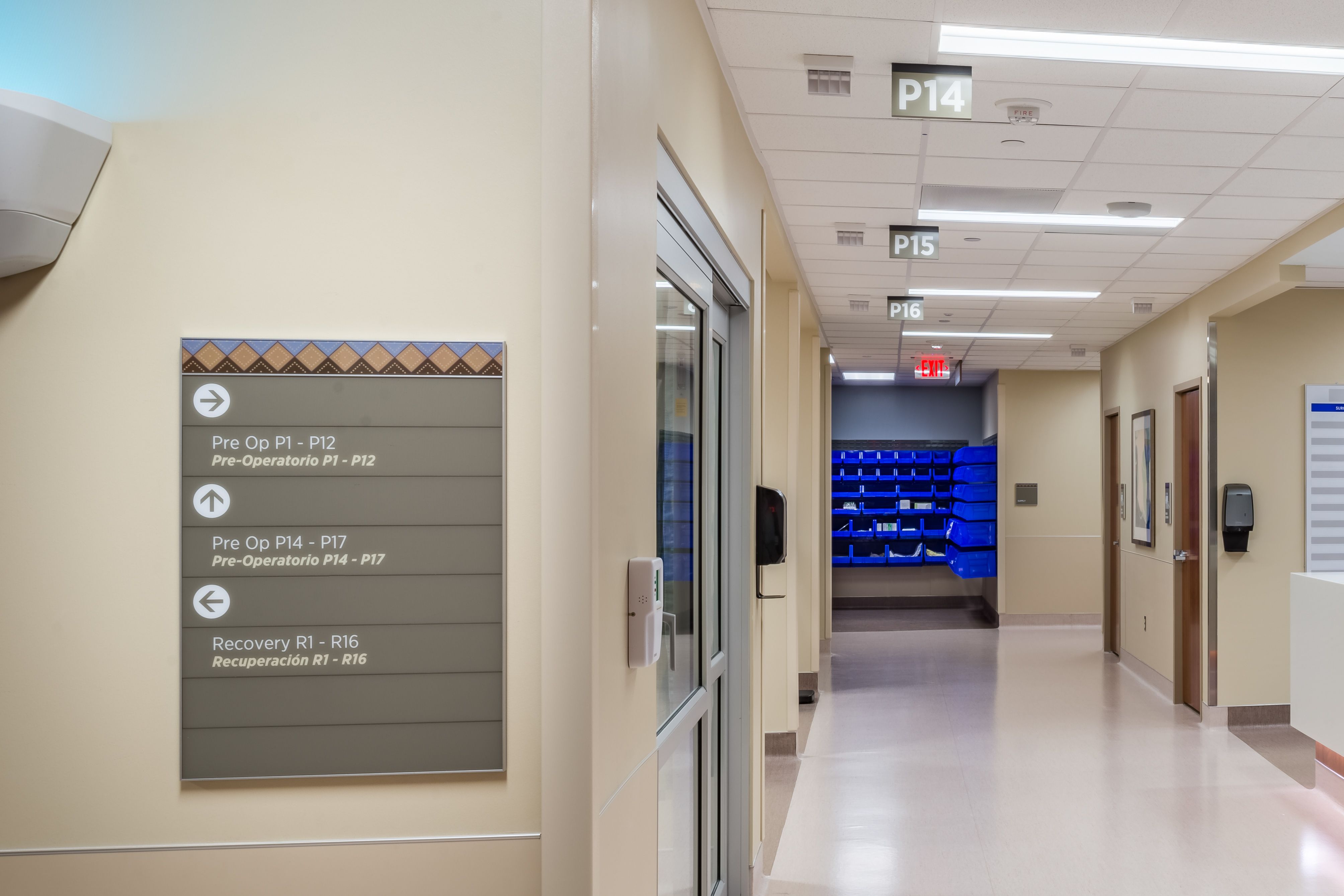 A brown wall directional sign with a southwest-inspired patterned header points to pre-op and recovery rooms in a hospital.