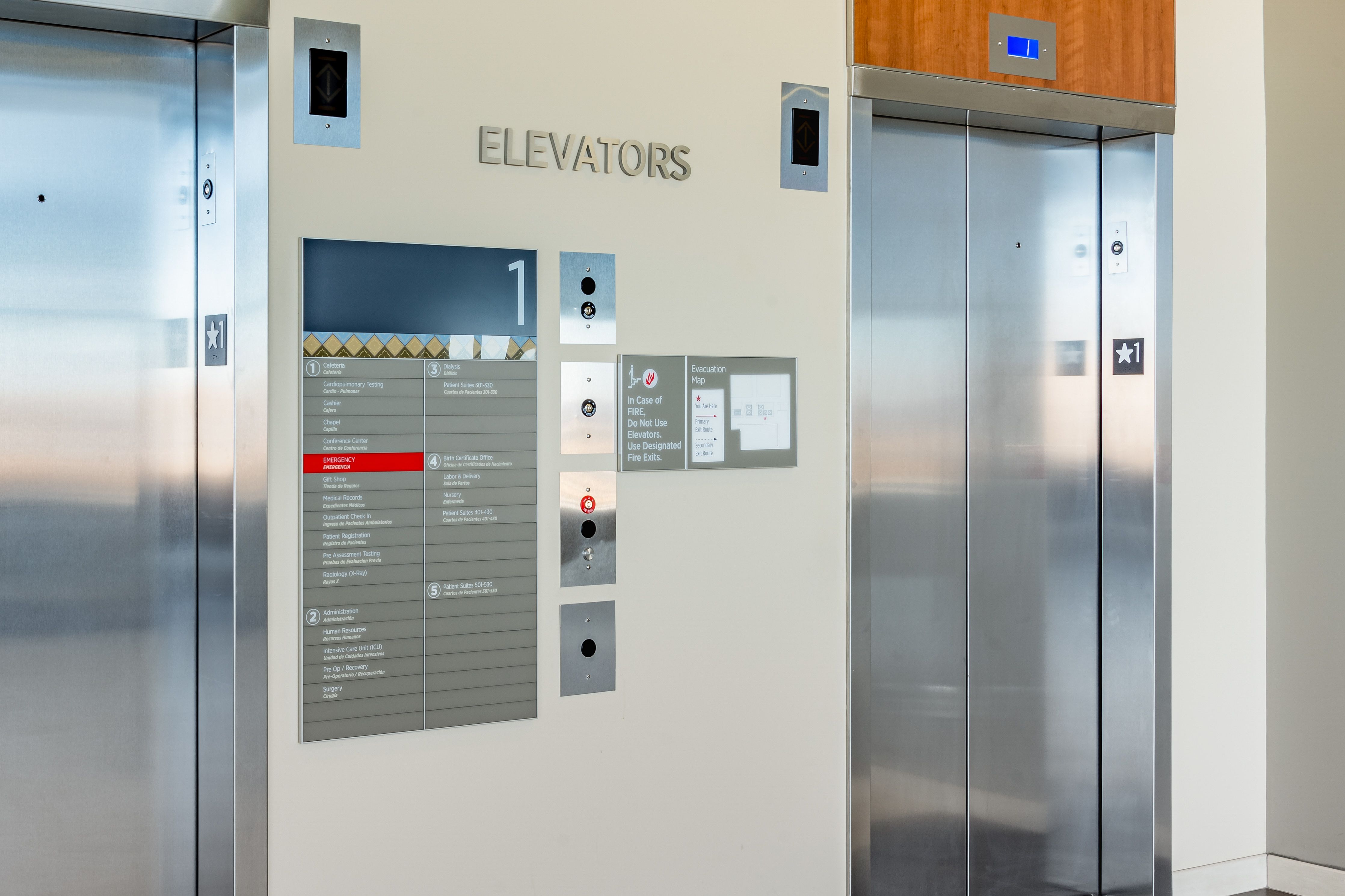 A pair of signs mounted at an elevator indicate the evacuation plan in case of emergency, and list the departments and levels of a hospital.