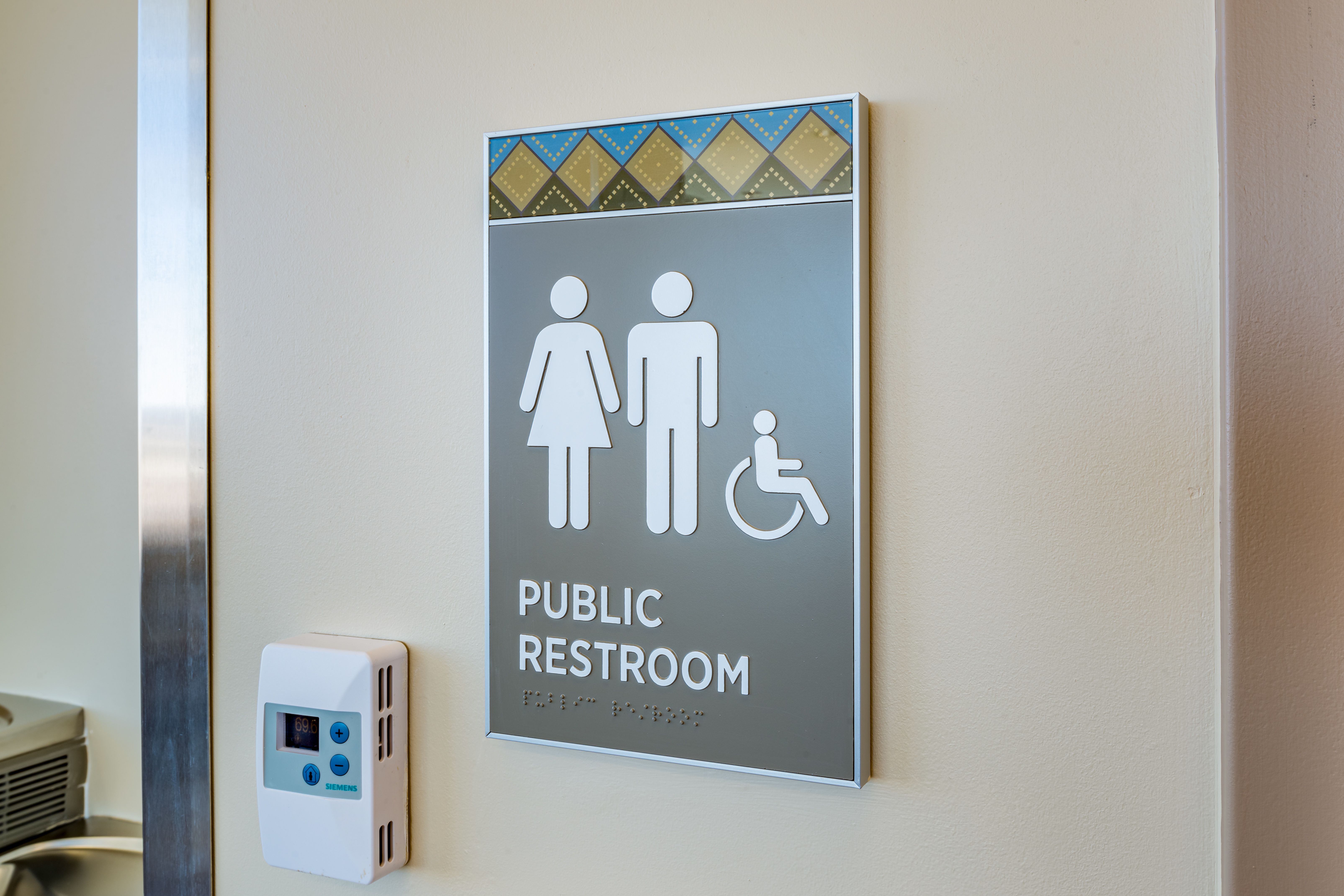 A room sign with tactile "PUBLIC RESTROOM" text, braille, symbols, and a southwest-inspired header pattern.