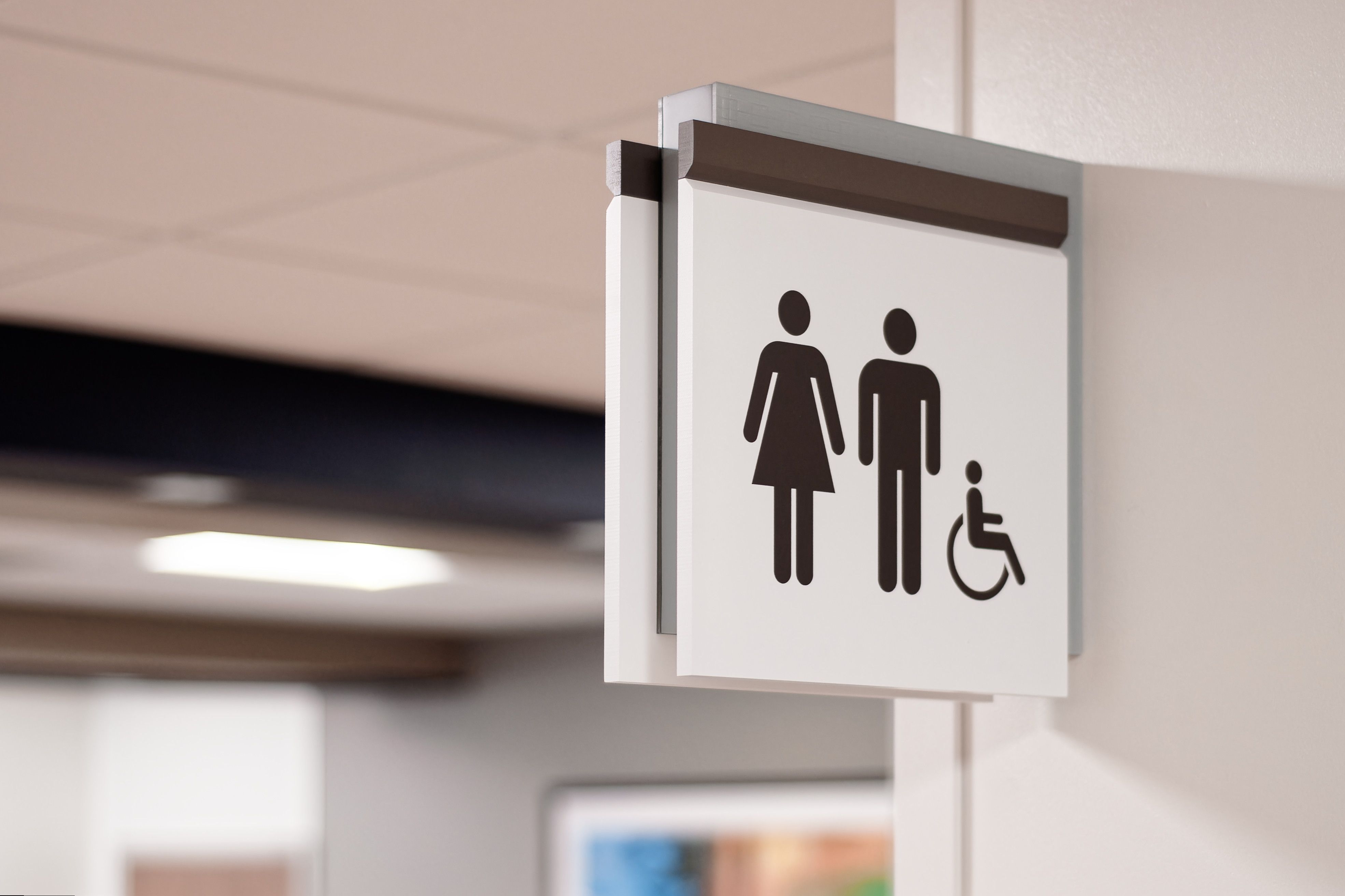 A projecting flag sign with restroom symbols is mounted in a hallway above a restroom.