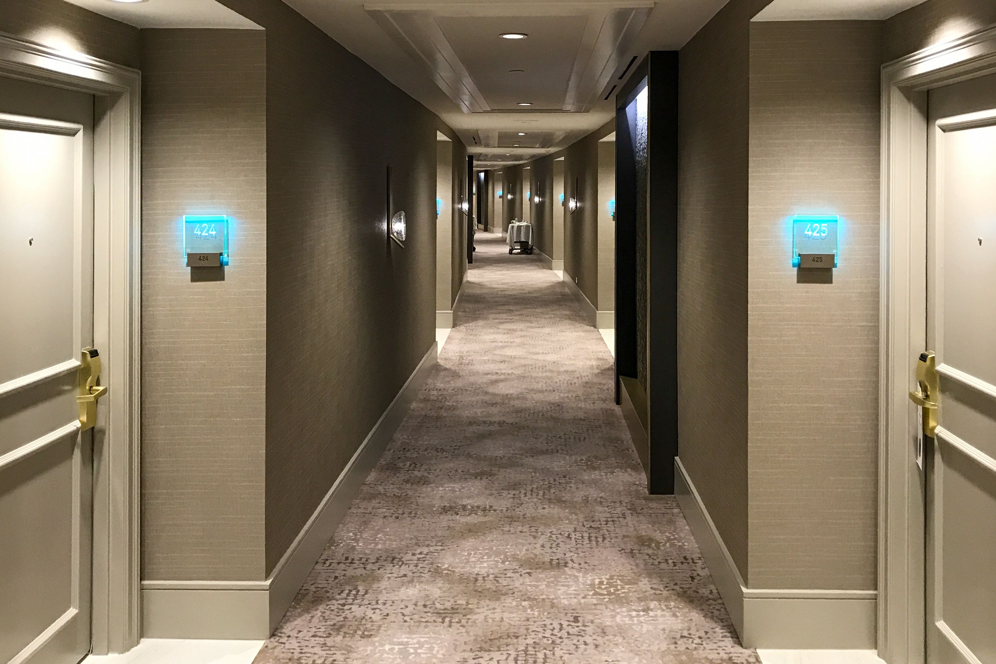 A hotel hallway with several tactile room signs featuring LED-illuminated acrylic panels etched with room numbers.