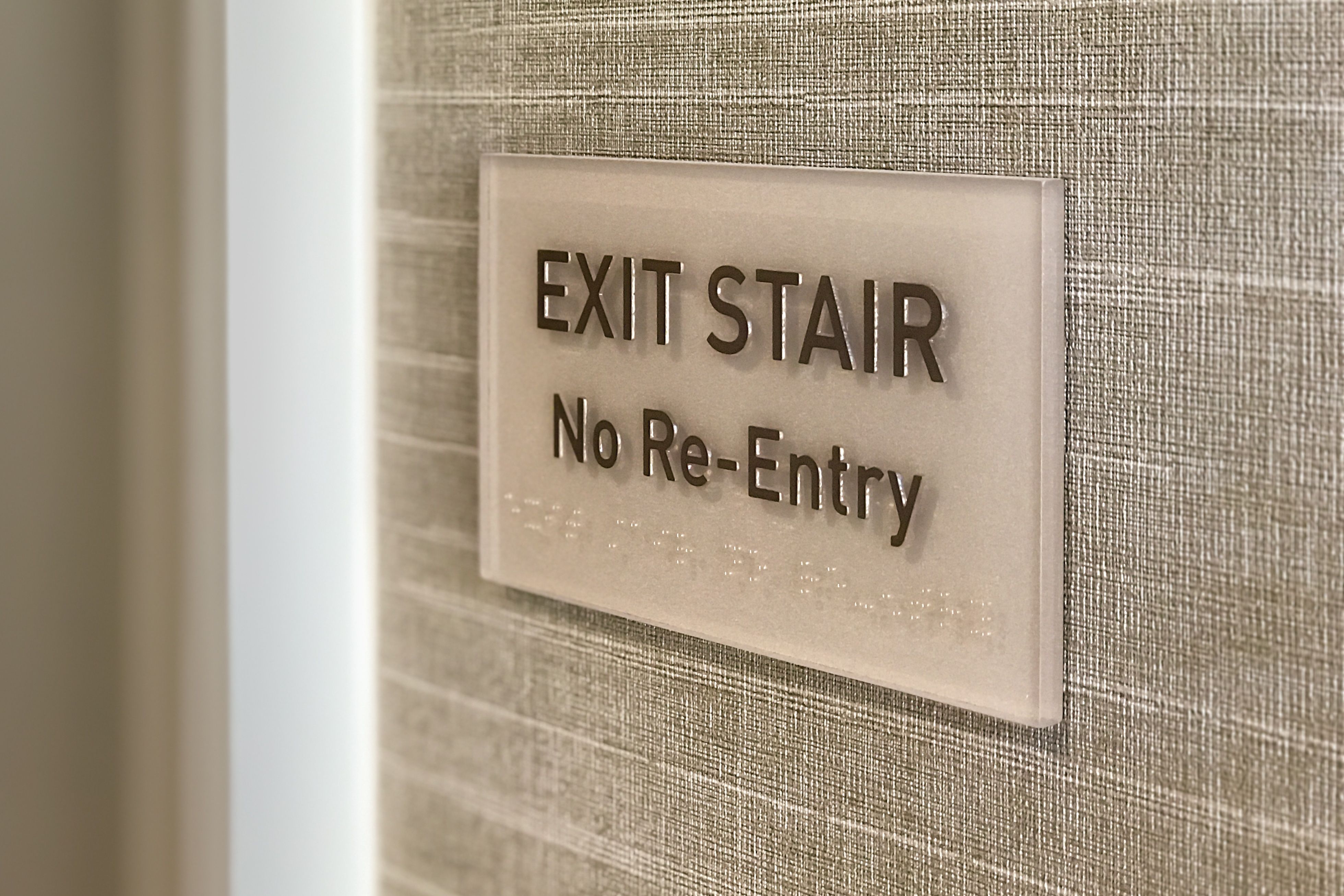 A photopolymer tactile "EXIT STAIR" sign mounted on a wall next to a stairwell door.