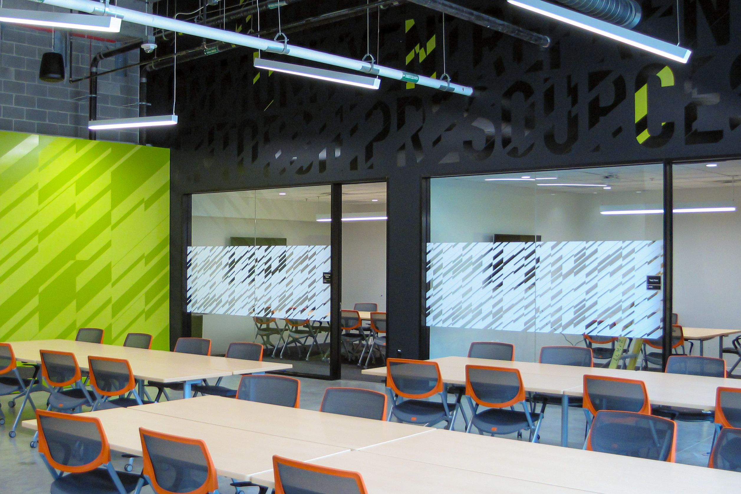 A large gathering space surrounded by classrooms is decorated with green and white vinyl patterns and lettering on the walls and glass.