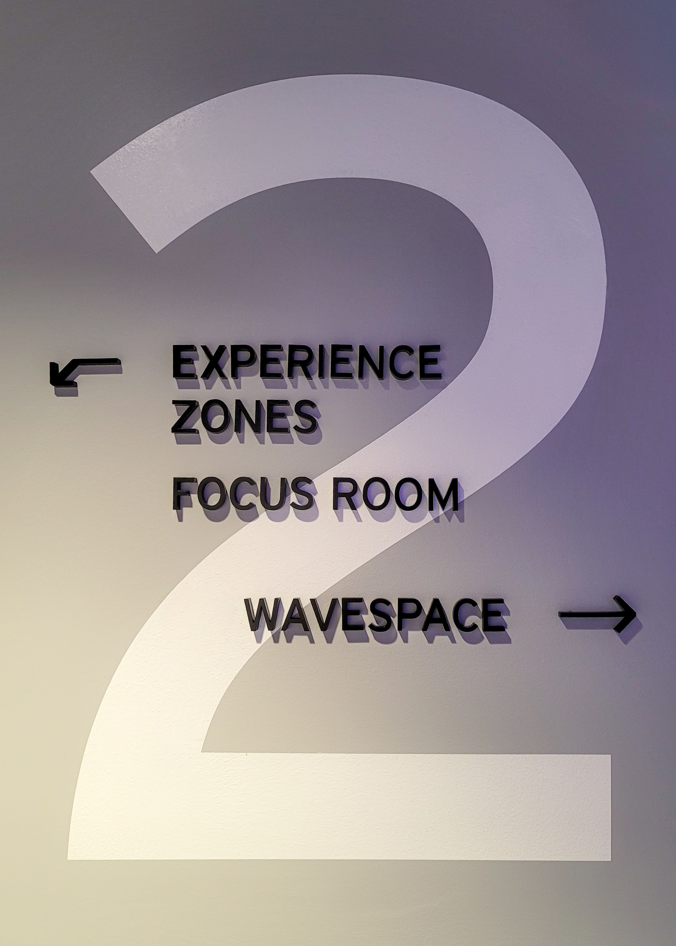 A large vinyl '2' is mounted to a wall, with black acrylic directional letters and arrows mounted on top, indicating various destinations.